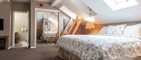 A bedroom with a large bed, skylight, ceiling fan, and a staircase leading to an upper level.