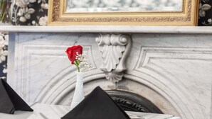 A table with black napkins, a red rose, and a white vase with baby's breath.