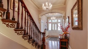 A grand staircase with ornate woodwork and a chandelier, leading to a door with stained glass windows.