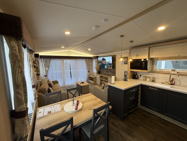 Cocina compacta con comedor, televisor y ventana con cortinas.