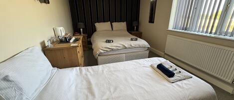 A hotel room with two beds, a wooden nightstand, a window with blinds, and a radiator.