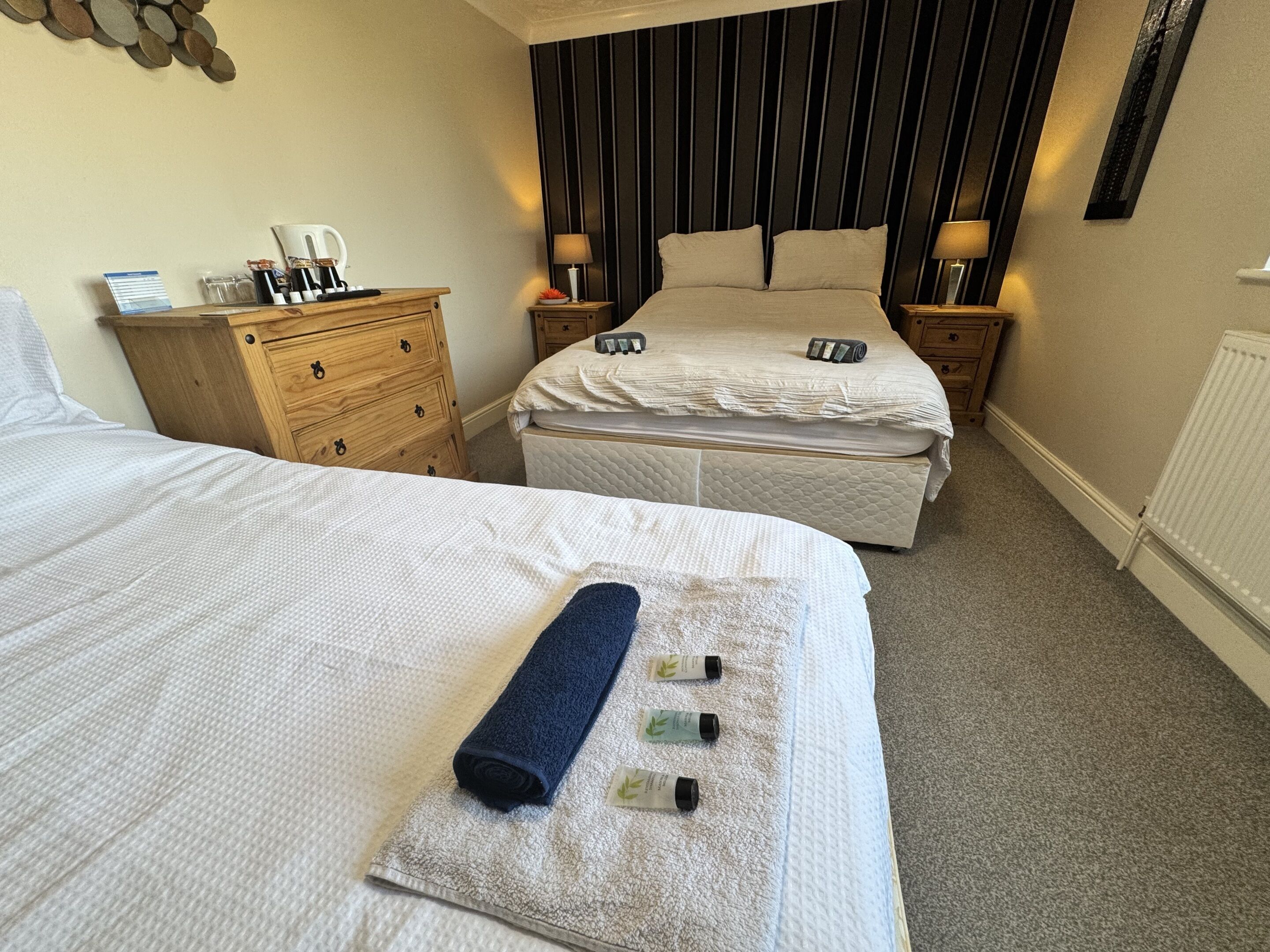 A hotel room with two beds, a wooden dresser, a nightstand, a lamp, and a wall-mounted artwork.