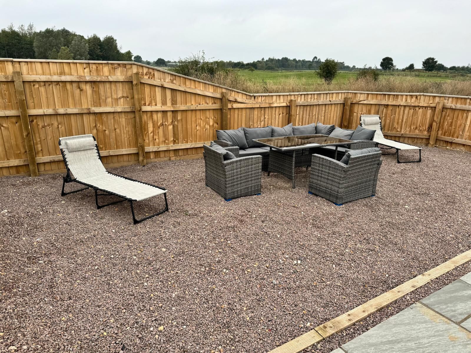 An outdoor patio with a wooden fence, a round table, and four grey wicker chairs.