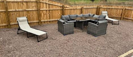 An outdoor patio with a wooden fence, a round table, and four grey wicker chairs.