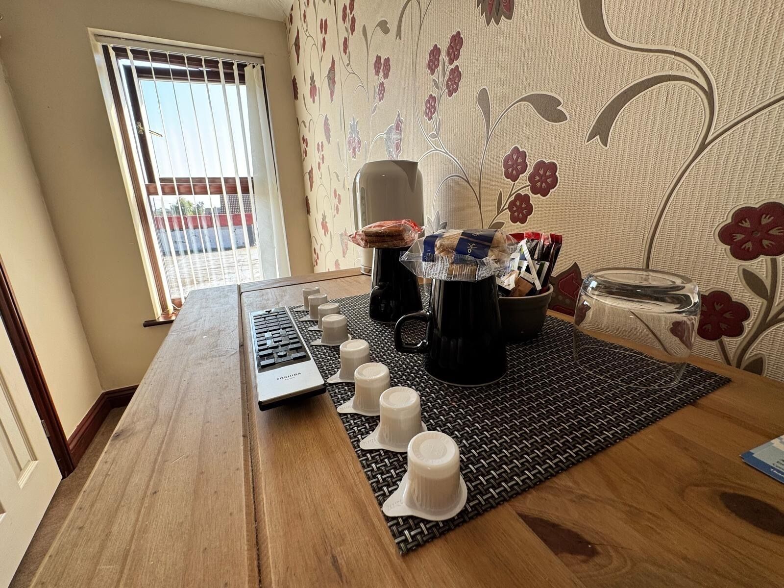 Une table en bois sur laquelle se trouvent un ordinateur portable, une machine à café et plusieurs tasses blanches.