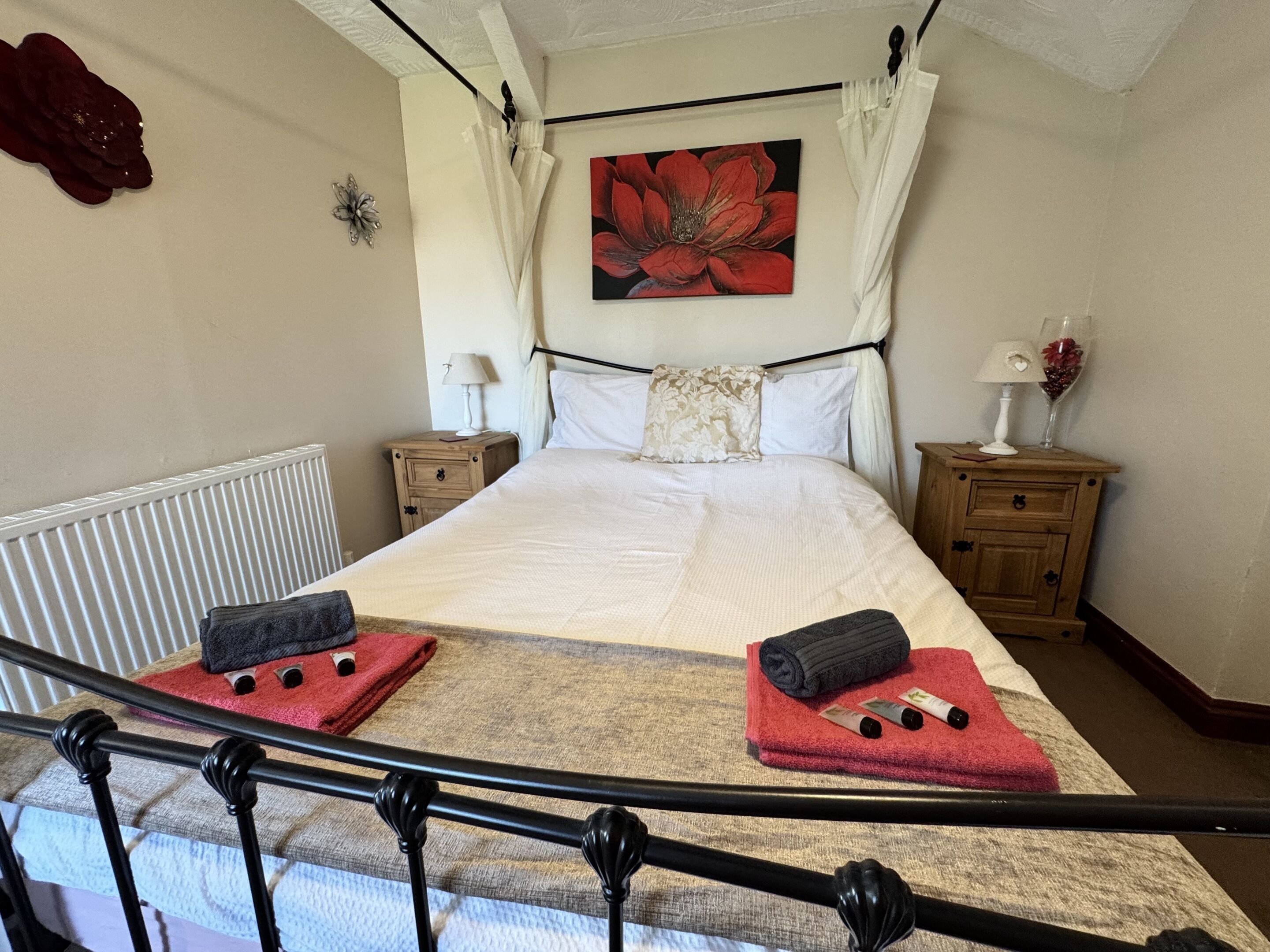 A neatly arranged bedroom with a large bed, two bedside tables, a nightstand, and a red flower decoration.