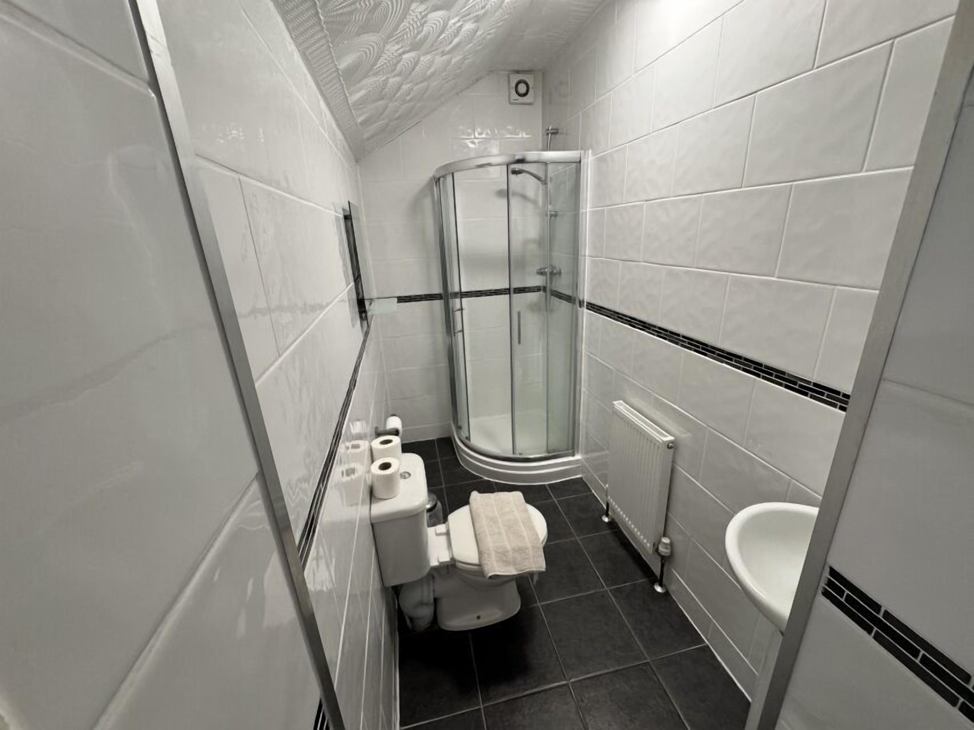 A modern bathroom with white tiles, a glass shower enclosure, a toilet, and a bidet.