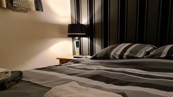 A neatly made bed with striped bedding, a folded towel, and a bedside lamp.