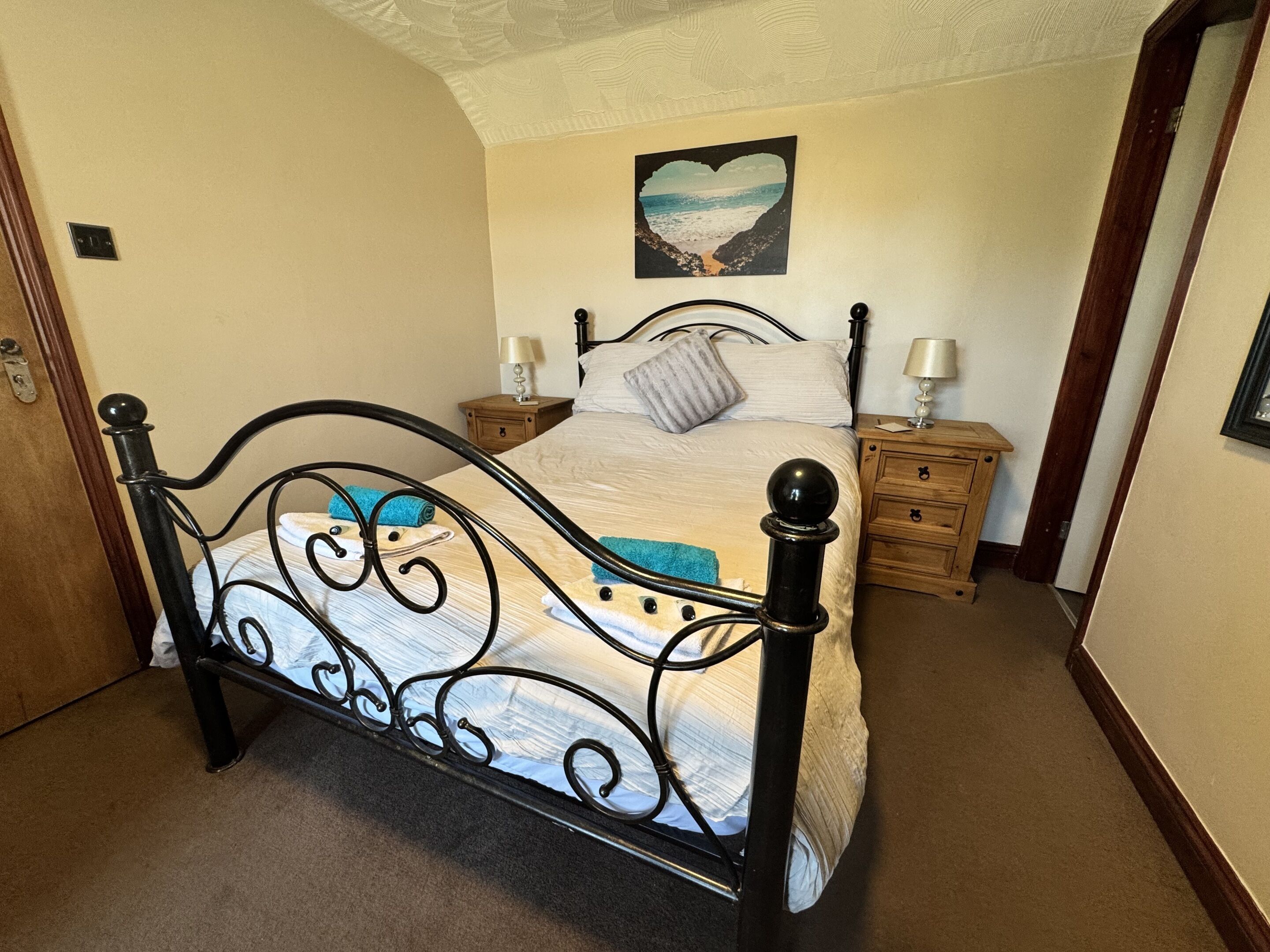 A bedroom with a four-poster bed, wooden nightstands, a night lamp, and a heart-shaped picture on the wall.