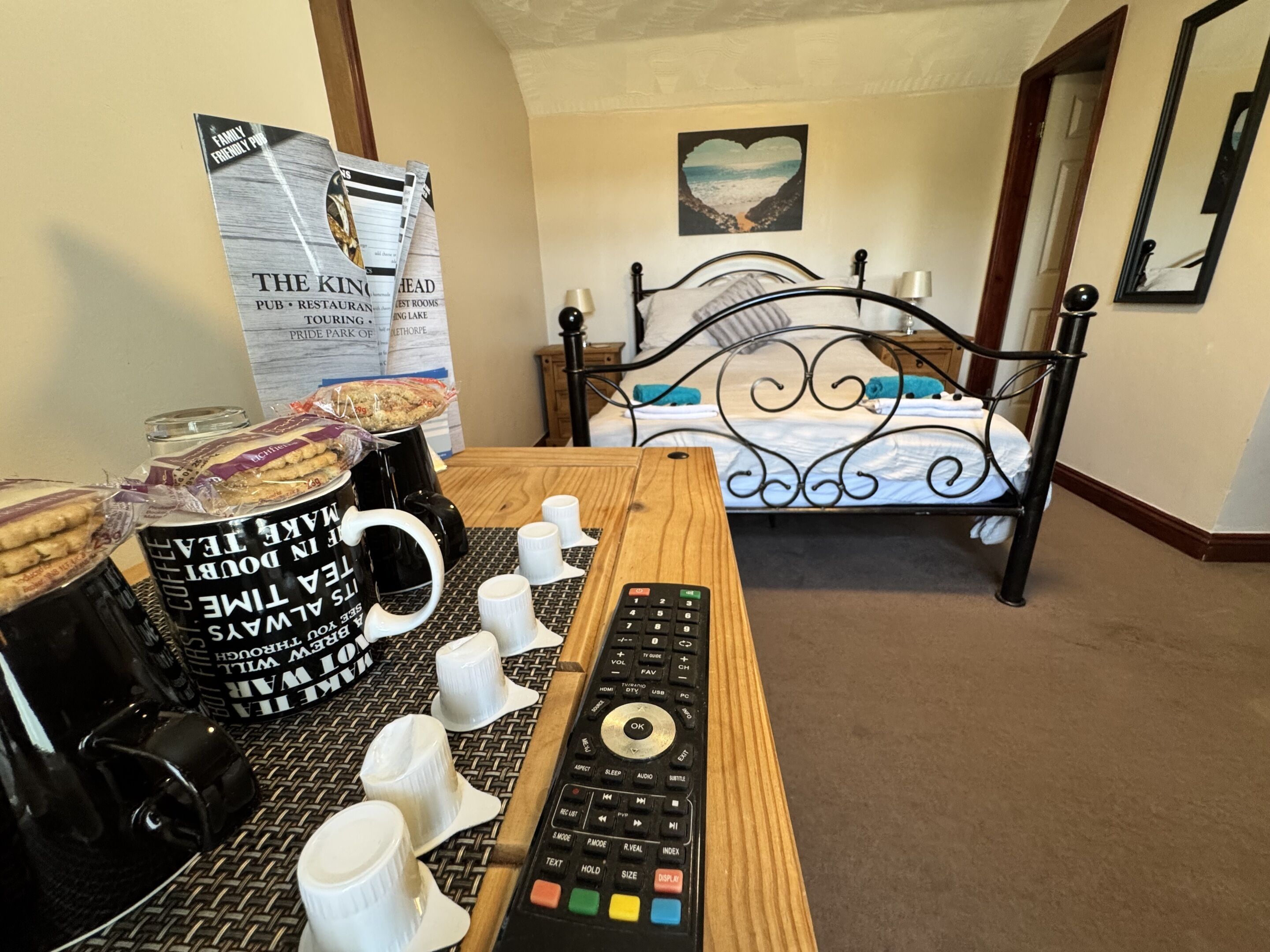 A hotel room with a bed, a coffee table with a remote control, and a newspaper on the wall.