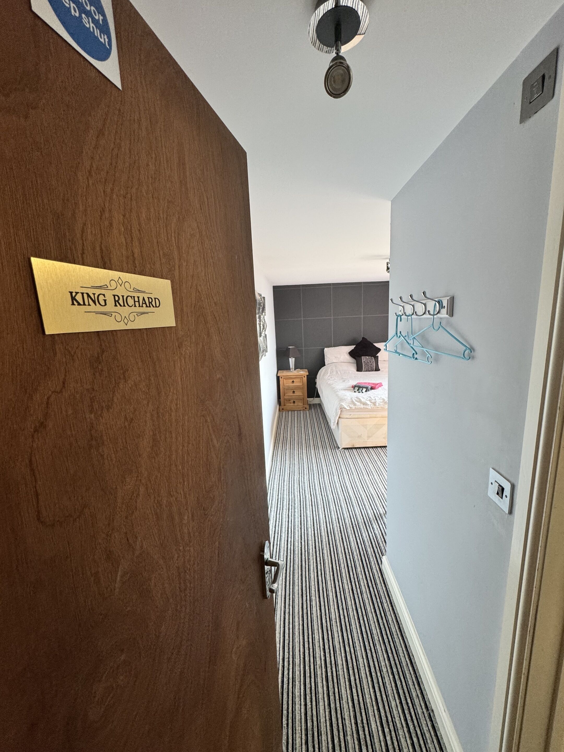Una habitación de hotel con cama, mesita de noche, lámpara y perchero en la pared.