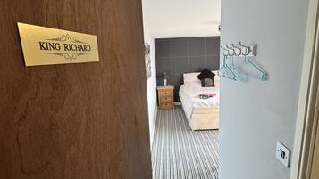 Una habitación de hotel con cama, mesita de noche, lámpara y perchero en la pared.