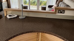 A modern kitchen with a granite countertop, wooden cabinets, and a view of a lake through large windows. - The Kings Head inn (Skegness)