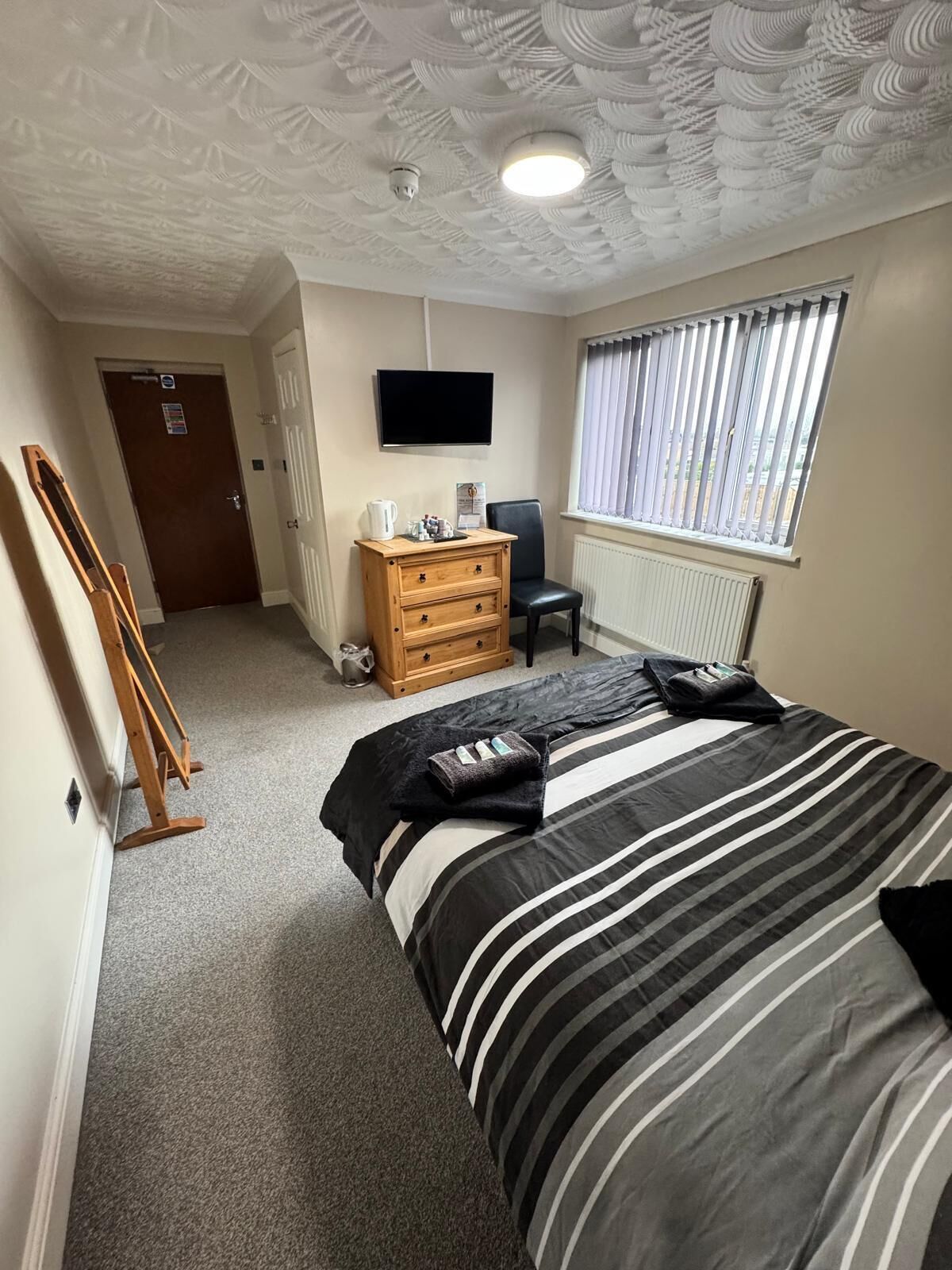 A bedroom with a bed, a wooden dresser, a television, and a window with blinds.