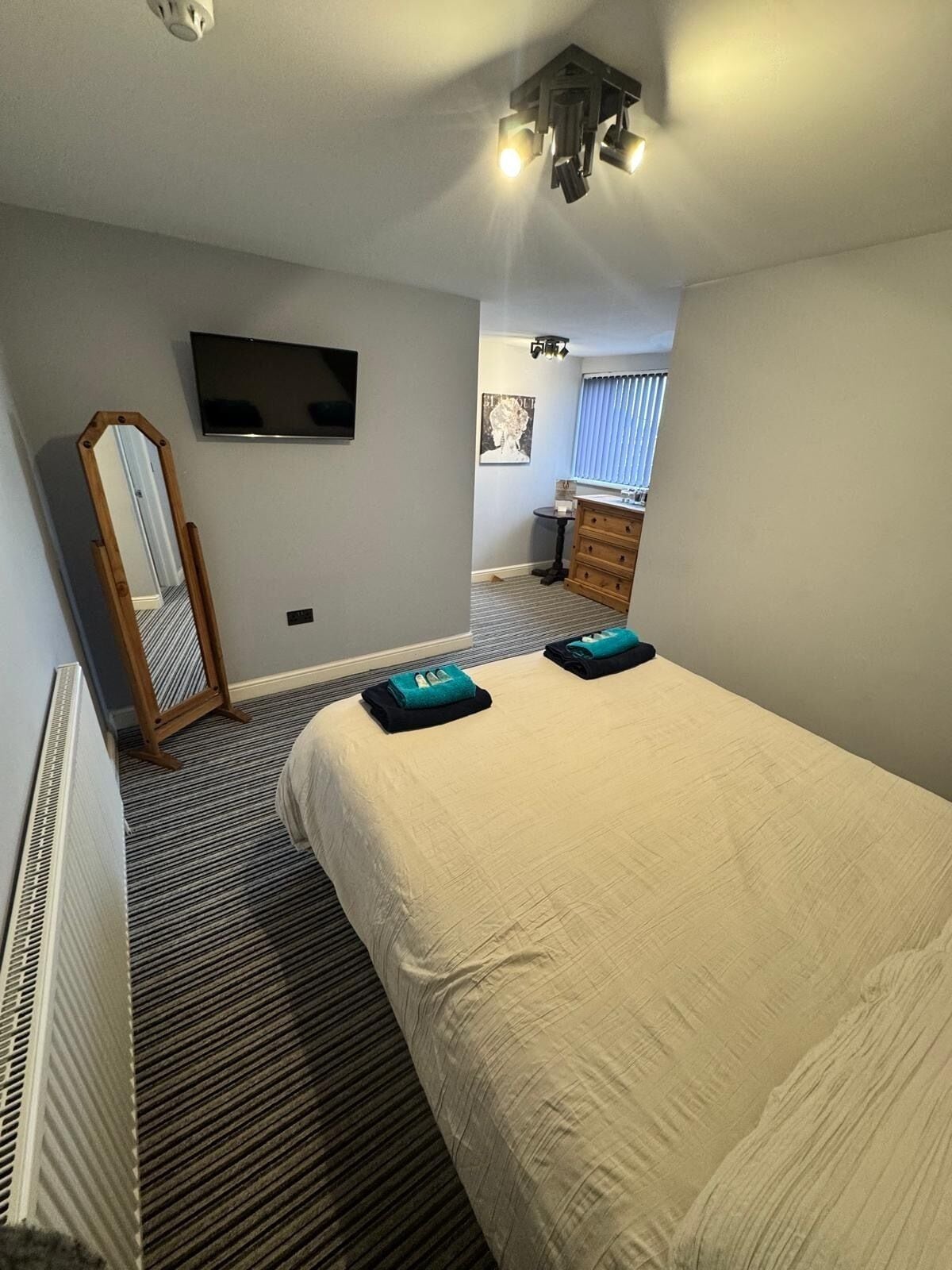 A hotel room with a bed, a dresser, a mirror, a television, and a ceiling light fixture.