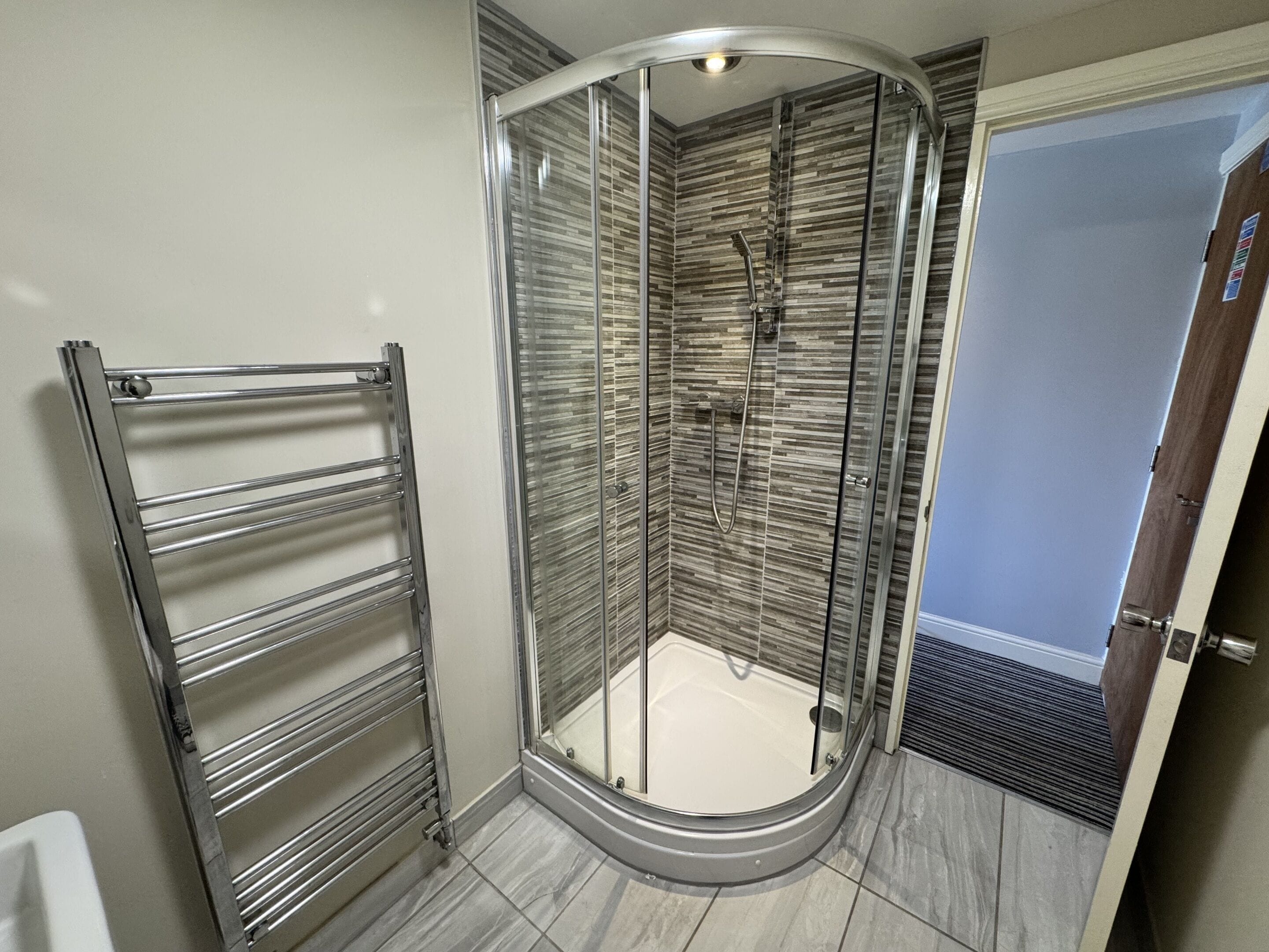 A modern bathroom with a glass-enclosed shower, a metal towel rack, and a tiled floor.