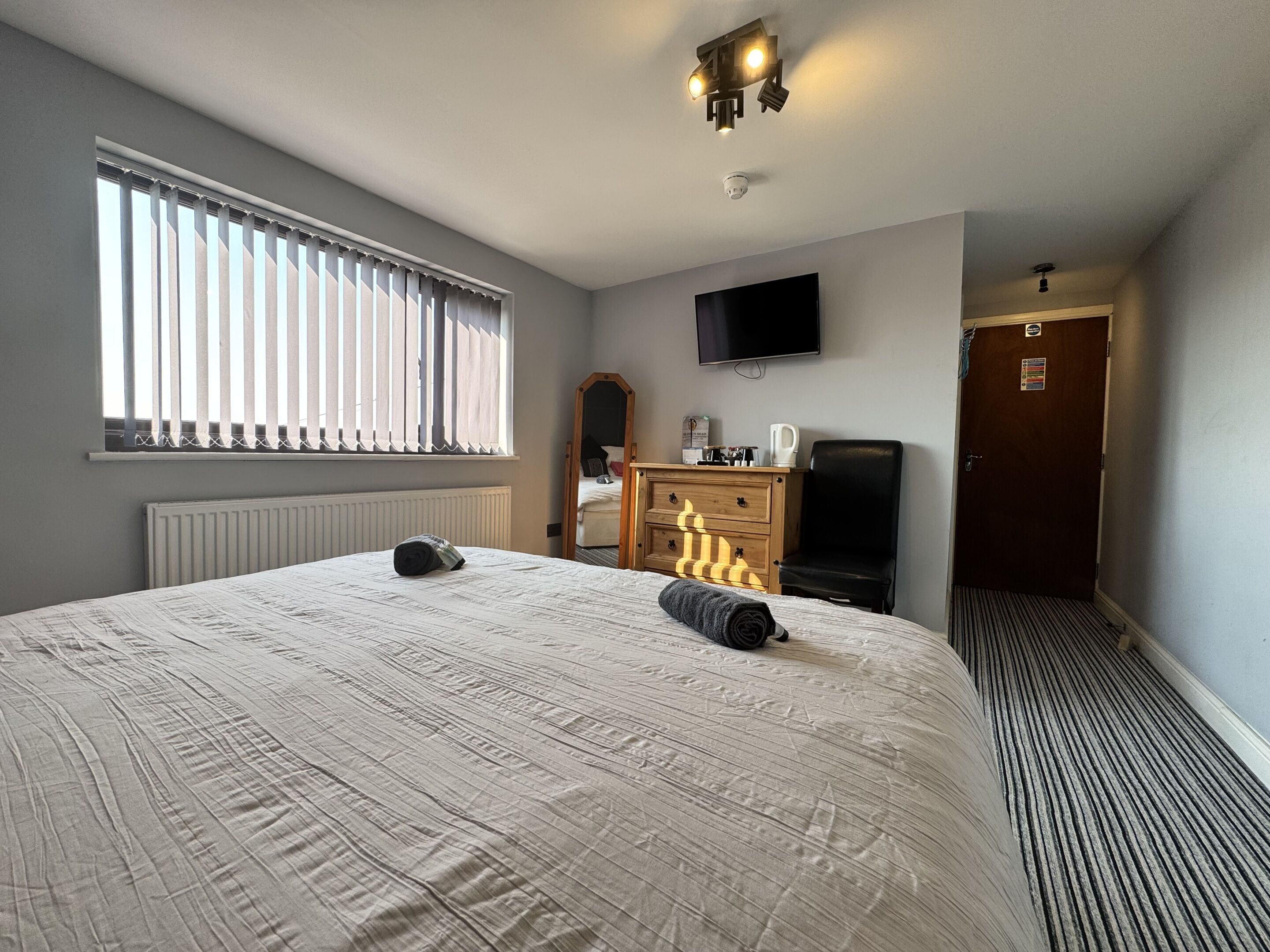 A hotel room with a large bed, a television, a dresser, and a door.