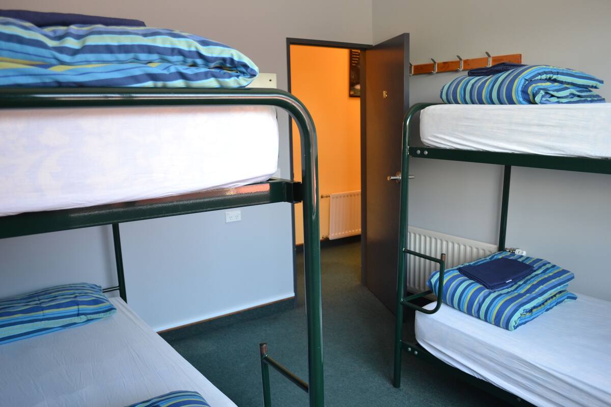 Een slaapzaal met stapelbedden, een radiator en een deur naar een andere kamer.