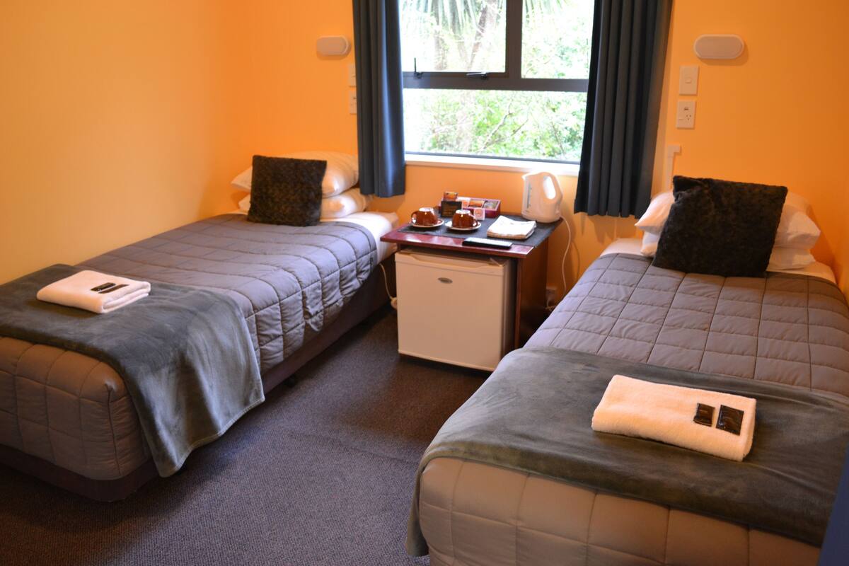 Een hotelkamer met twee bedden, een klein tafeltje met een waterkoker en een raam met gordijnen.