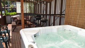 Un bain à remous sur une terrasse en bois, agrémentée d’une clôture en bambou et de mobilier d’extérieur.