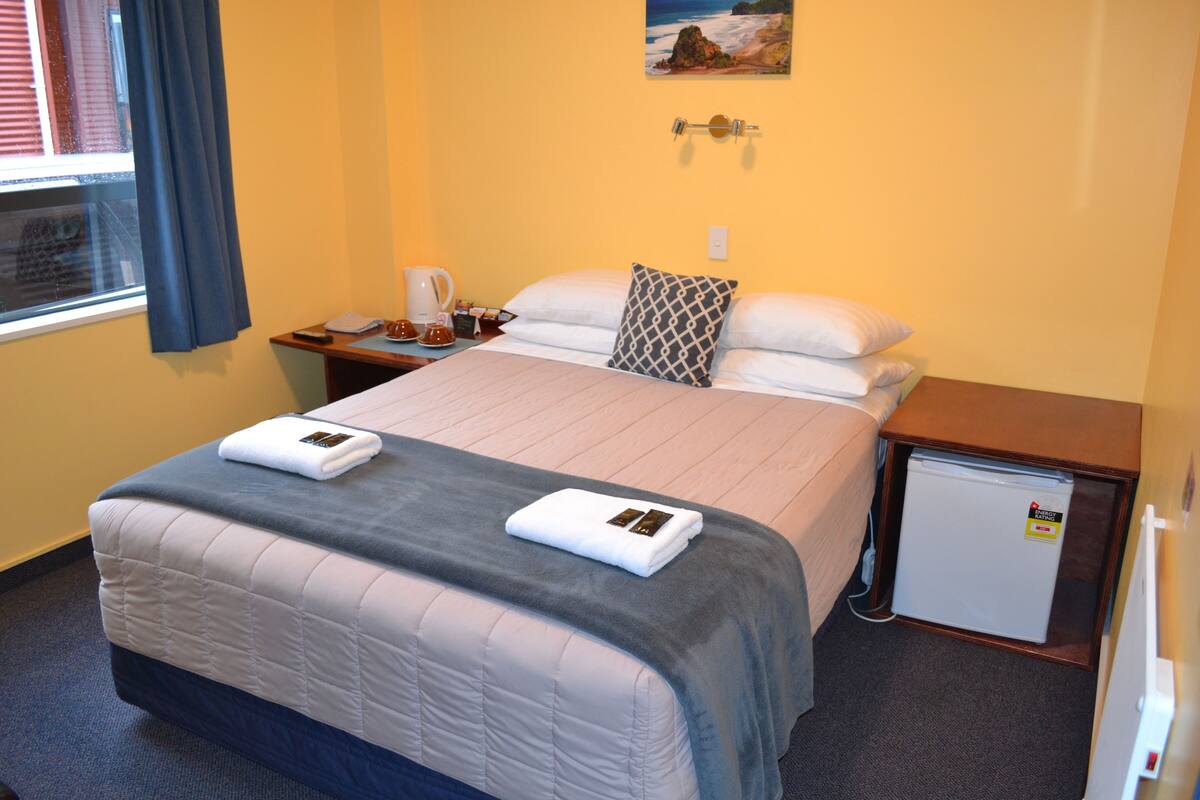 Een hotelkamer met een bed, een nachtkastje, een kleine koelkast en een raam met gordijnen.