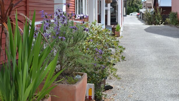 Un bâtiment rouge doté d’un porche, de plantes en pot et d’une allée gravillonnée.