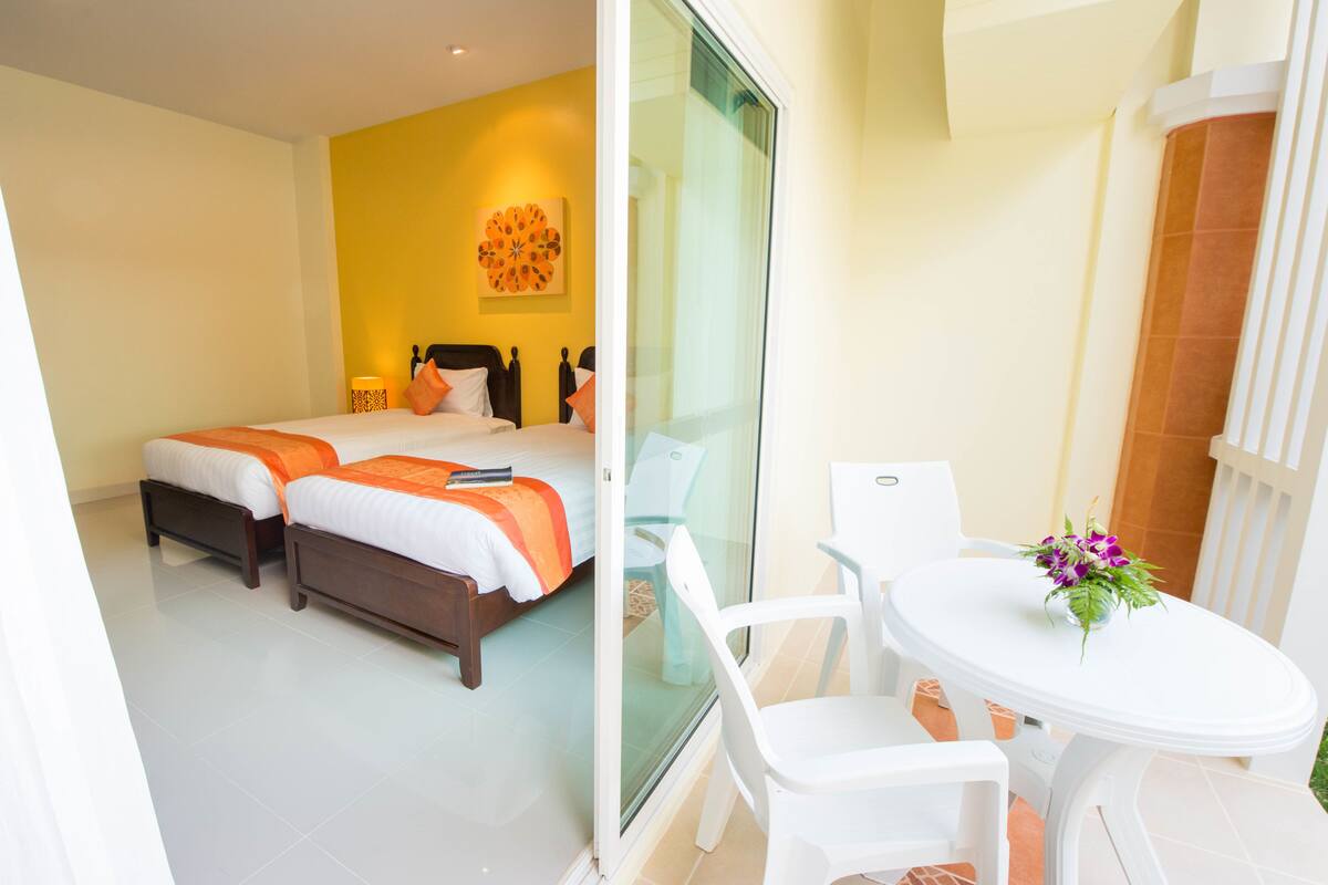 A hotel room with two beds, a glass door leading to an outdoor area with a white table and chairs, and a decorative wall piece.