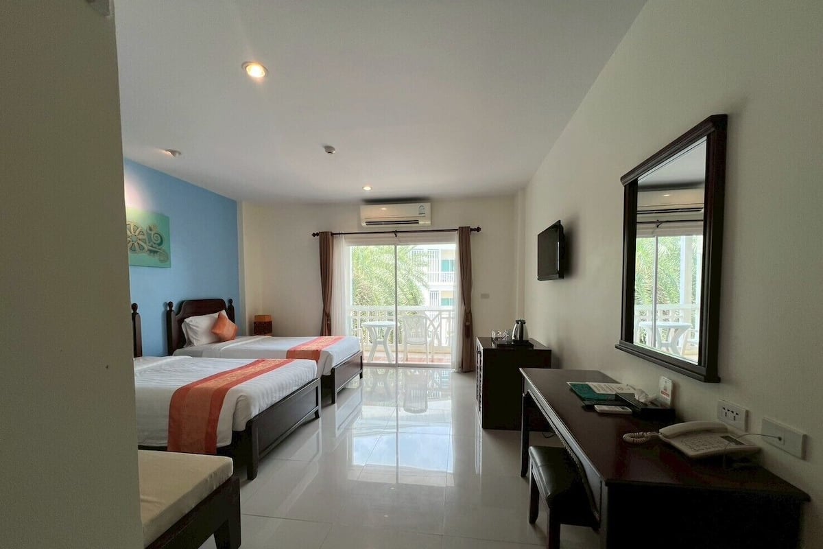 A hotel room with two beds, a desk, a chair, a TV, and a balcony with a view.
