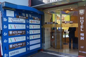 A hotel entrance with a blue directory board listing room numbers and amenities.
