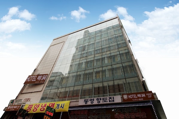 A modern hotel building with reflective glass windows and multiple signs, including one for the front desk.