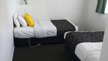 A small, compact room with two single beds, a gray abstract painting on the wall, a green curtain, and a white wall socket.