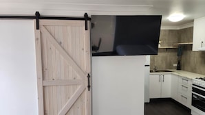 Cuina amb armaris blancs, fornell negre i una porta corredissa de graner.