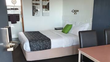 A hotel room with a bed, a desk, a chair, a small table, a ceiling fan, and a wall-mounted light.