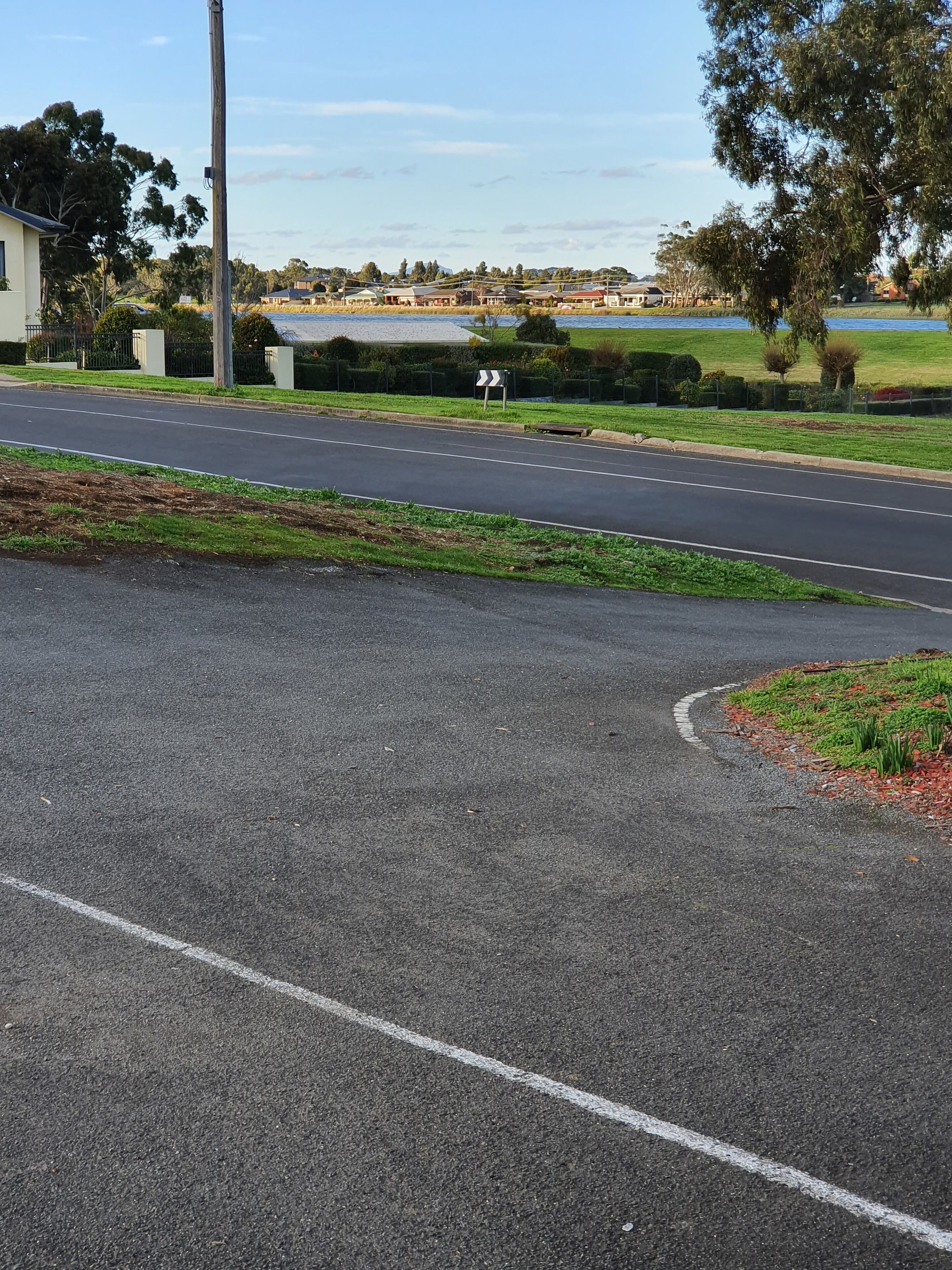 A road with a curve, a grassy area, and a body of water in the background.