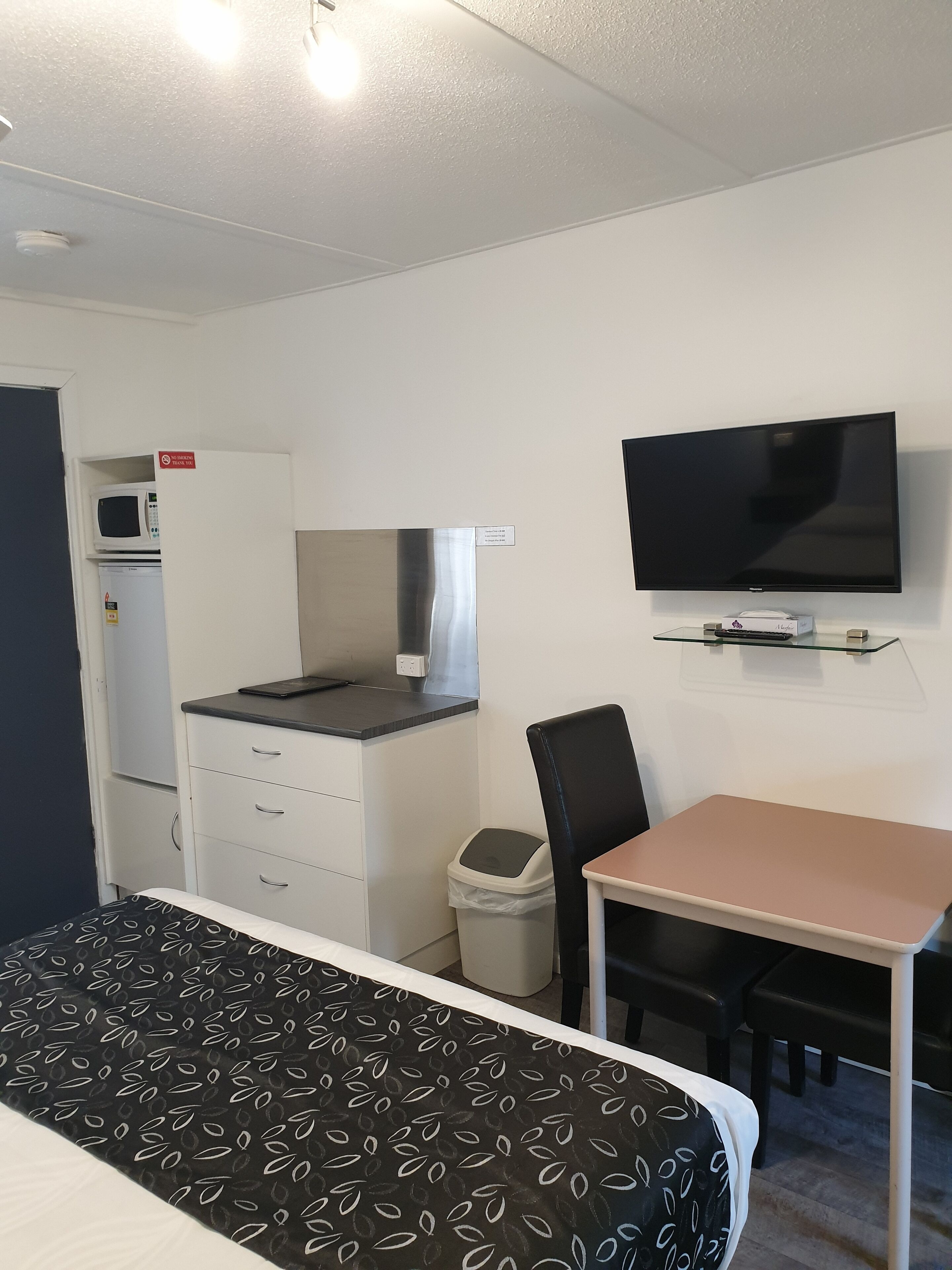 Habitación de hotel con cama, escritorio, silla, televisor, microondas y refrigerador.