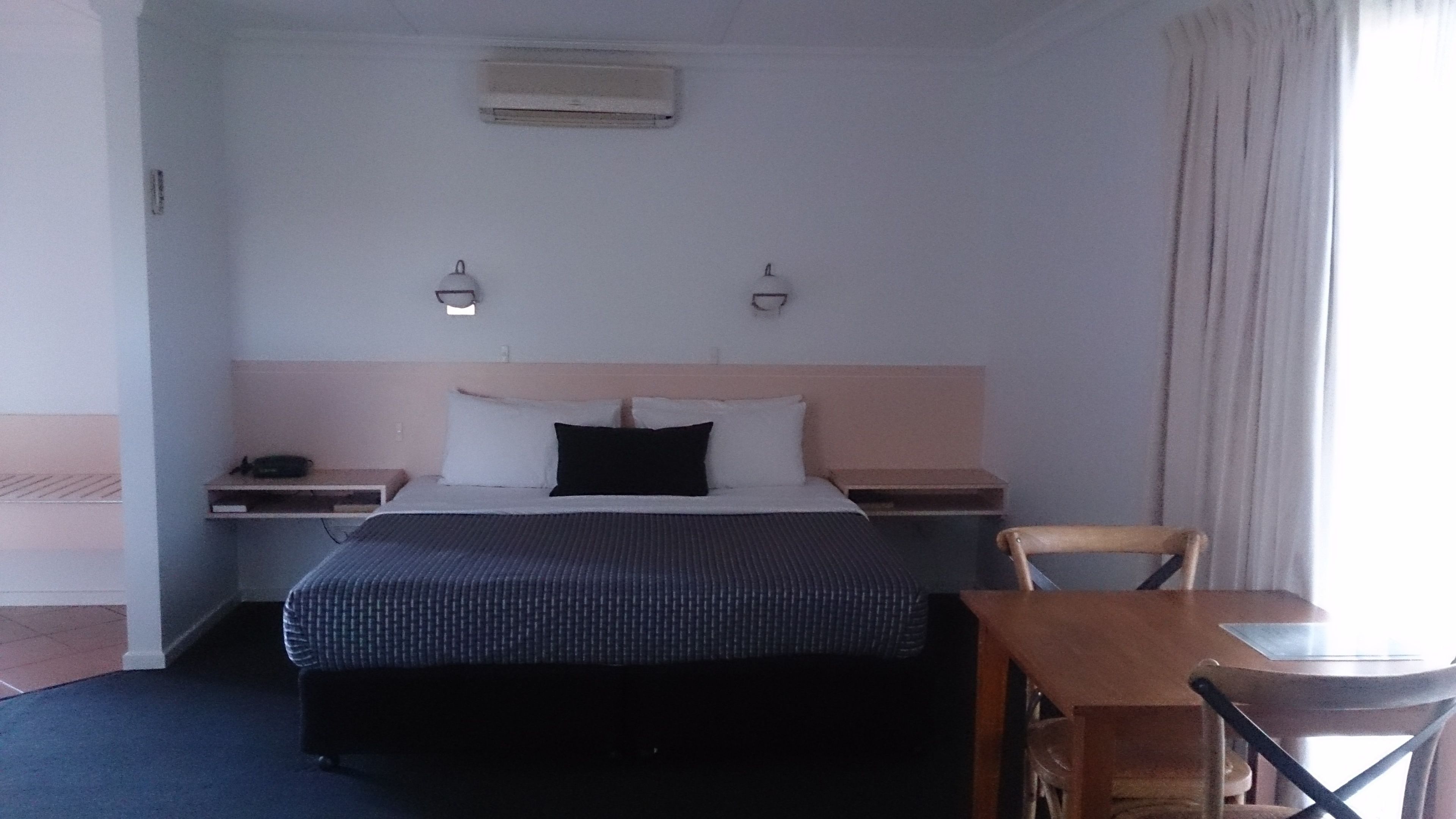 Ein Hotelzimmer mit einem Bett, Nachttischen, einem Sessel, einem Tisch und einer Klimaanlage an der Wand.