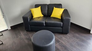 Un sofà de cuir negre amb dos coixins grocs en un angle d'una habitació amb sòl de fusta fosca.