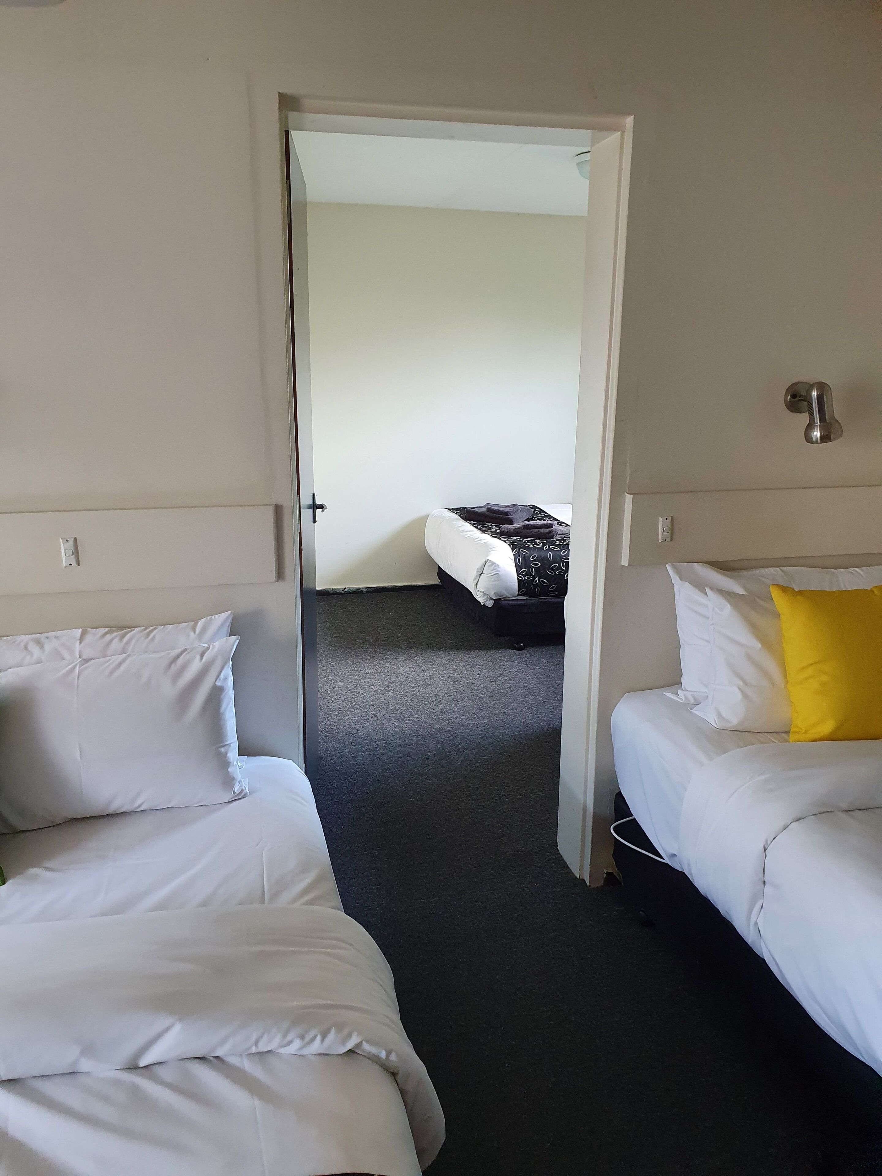 A hotel room with two single beds, a door leading to another room, and a carpeted floor.