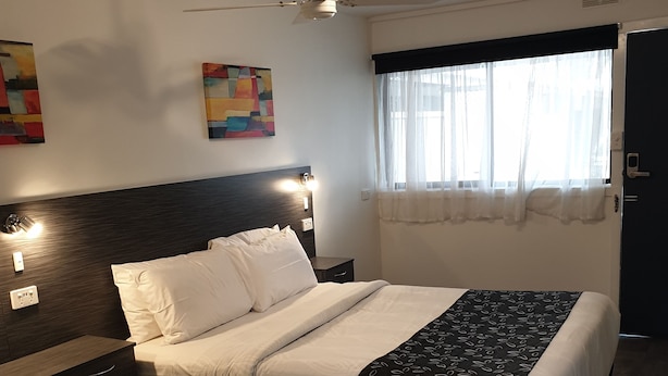 Habitació d'hotel amb llit, taula de nit i finestra amb cortines.