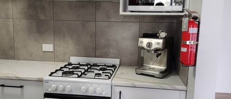 Una cocina con armarios blancos, estufa a gas, horno, máquina de café y extintor.