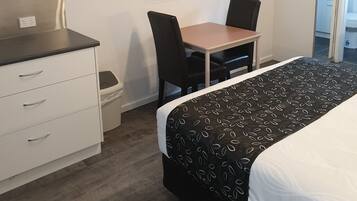 Une chambre d’hôtel comprenant un lit, un bureau avec une chaise, un téléviseur fixé au mur, une armoire et une poubelle.