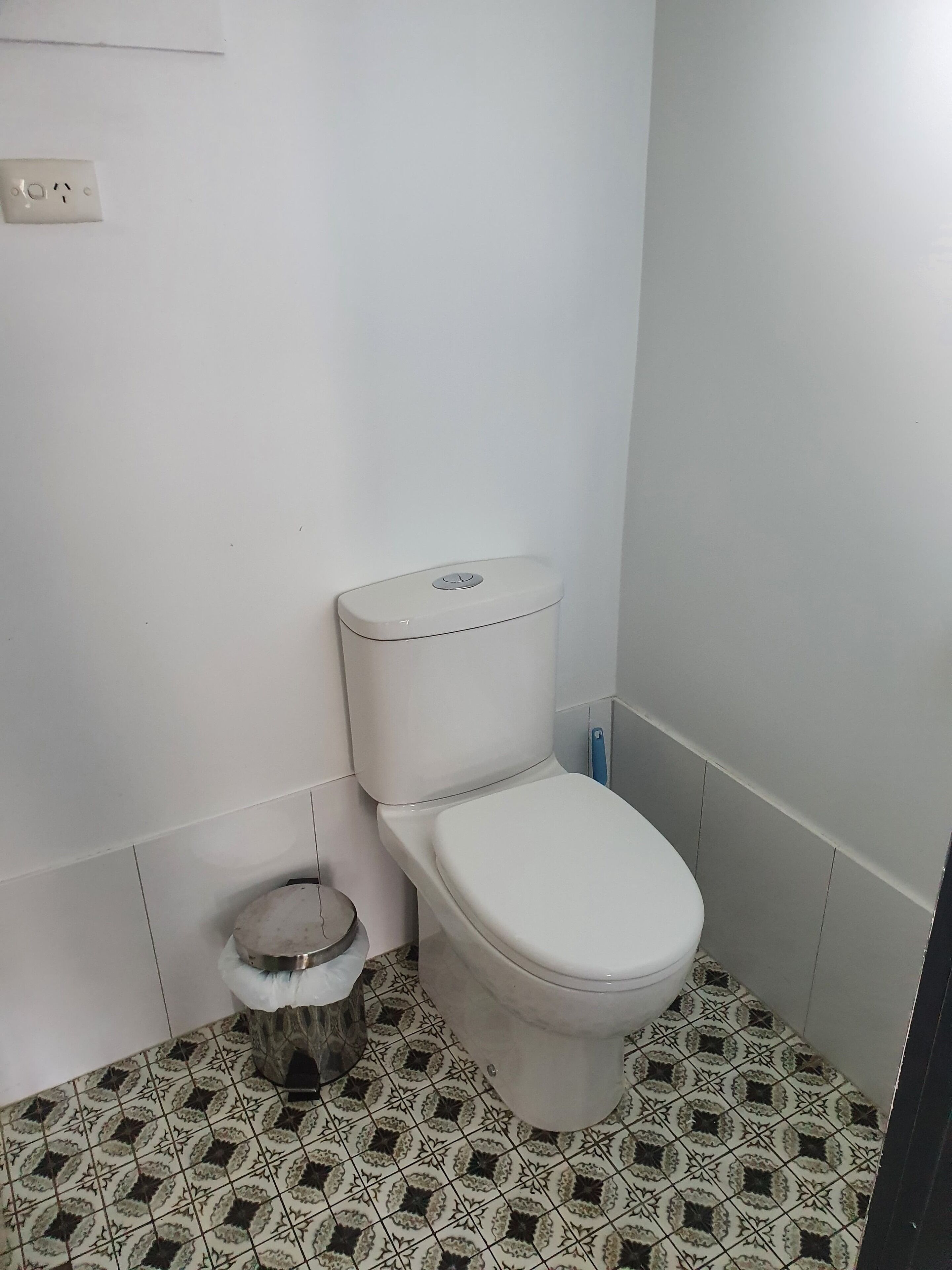 A small, clean bathroom with a white toilet, a small trash bin, and patterned floor tiles.