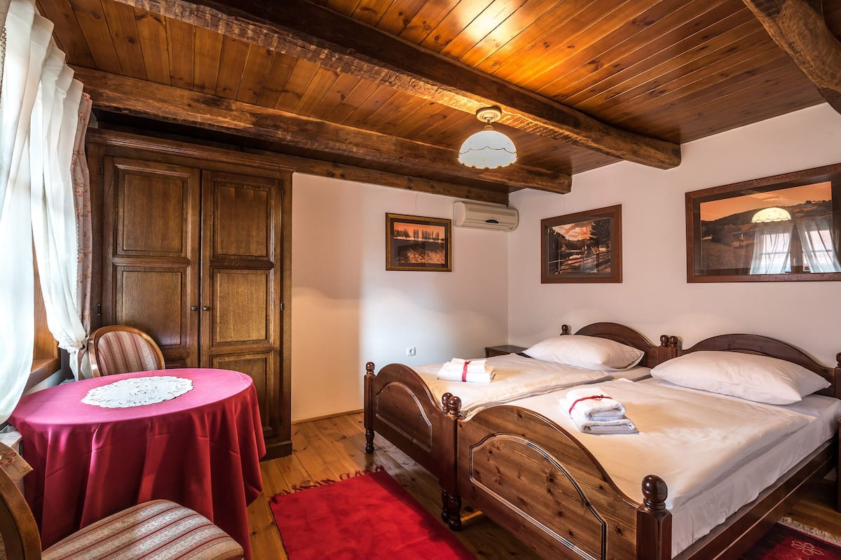Una habitación con dos camas de madera, techo de madera, una mesa con mantel rojo y una silla.