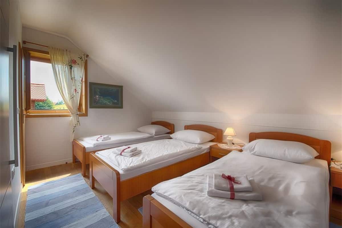 Un dormitorio con dos camas individuales, cabecera de madera, mesita de noche, lámpara de noche y una ventana con cortinas.