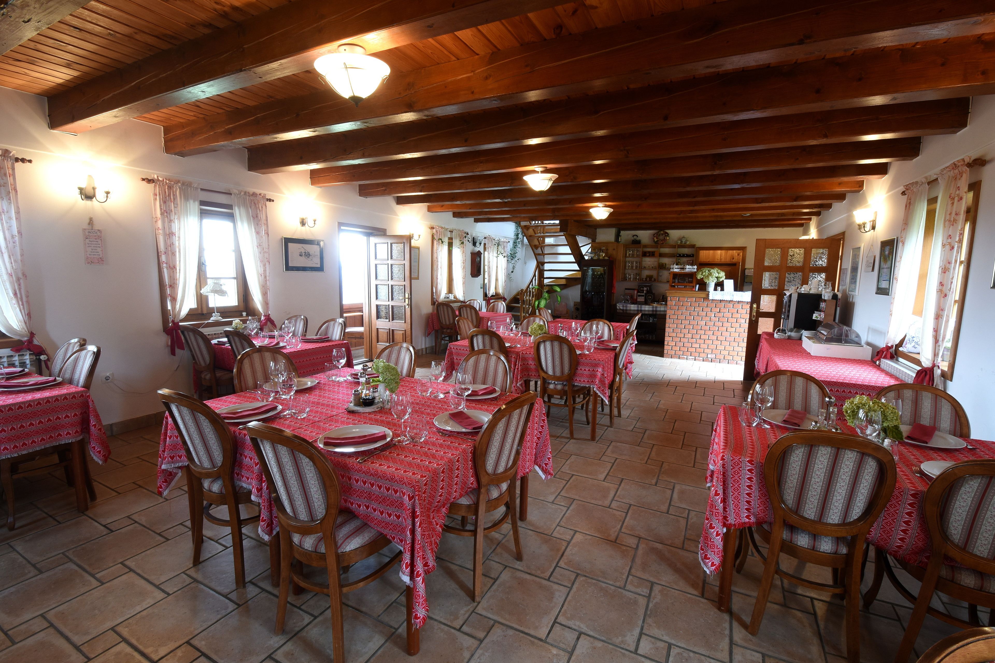 A dining area with multiple tables set for meals, wooden chairs, and a brick wall in the background.