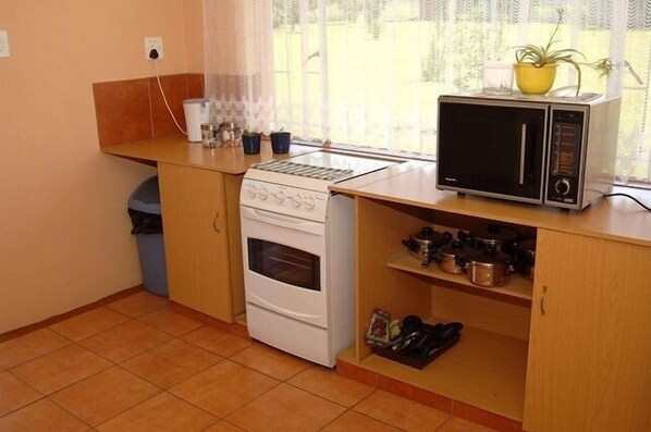 Cocina compacta con estufa, microondas y estanterías para utensilios.
