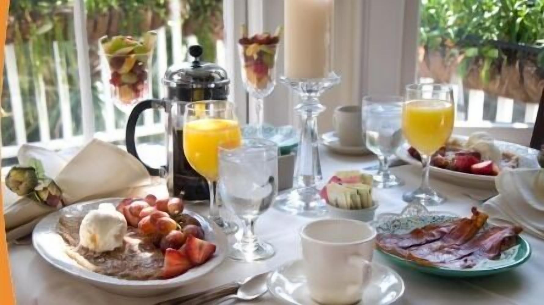 A breakfast setting with a variety of food items, including eggs, bacon, and fruit, along with beverages and a coffee maker.