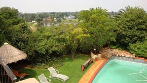 Zona de piscina con sillas de descanso, una estructura de techo de paja y vistas a un lago y edificios a lo lejos.