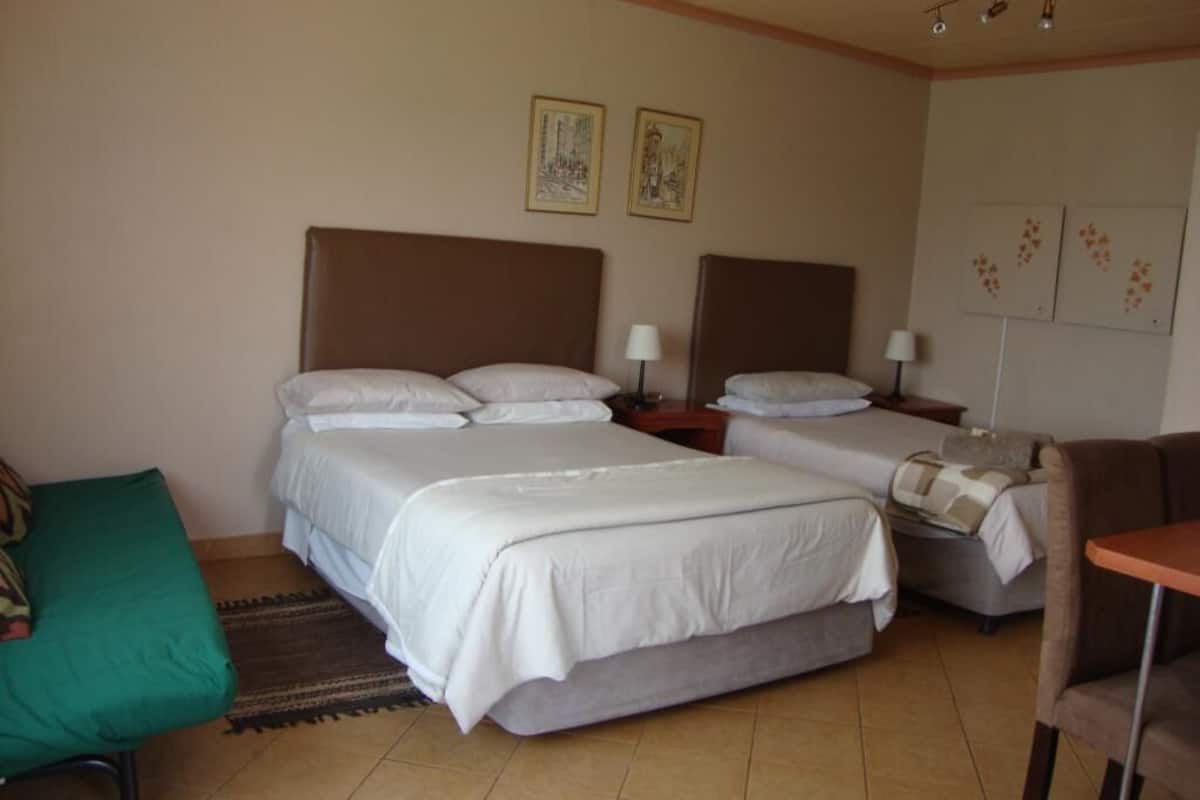 Habitació d'hotel amb dos llits, una cadira verda, una taula petita i obres d'art a les parets.