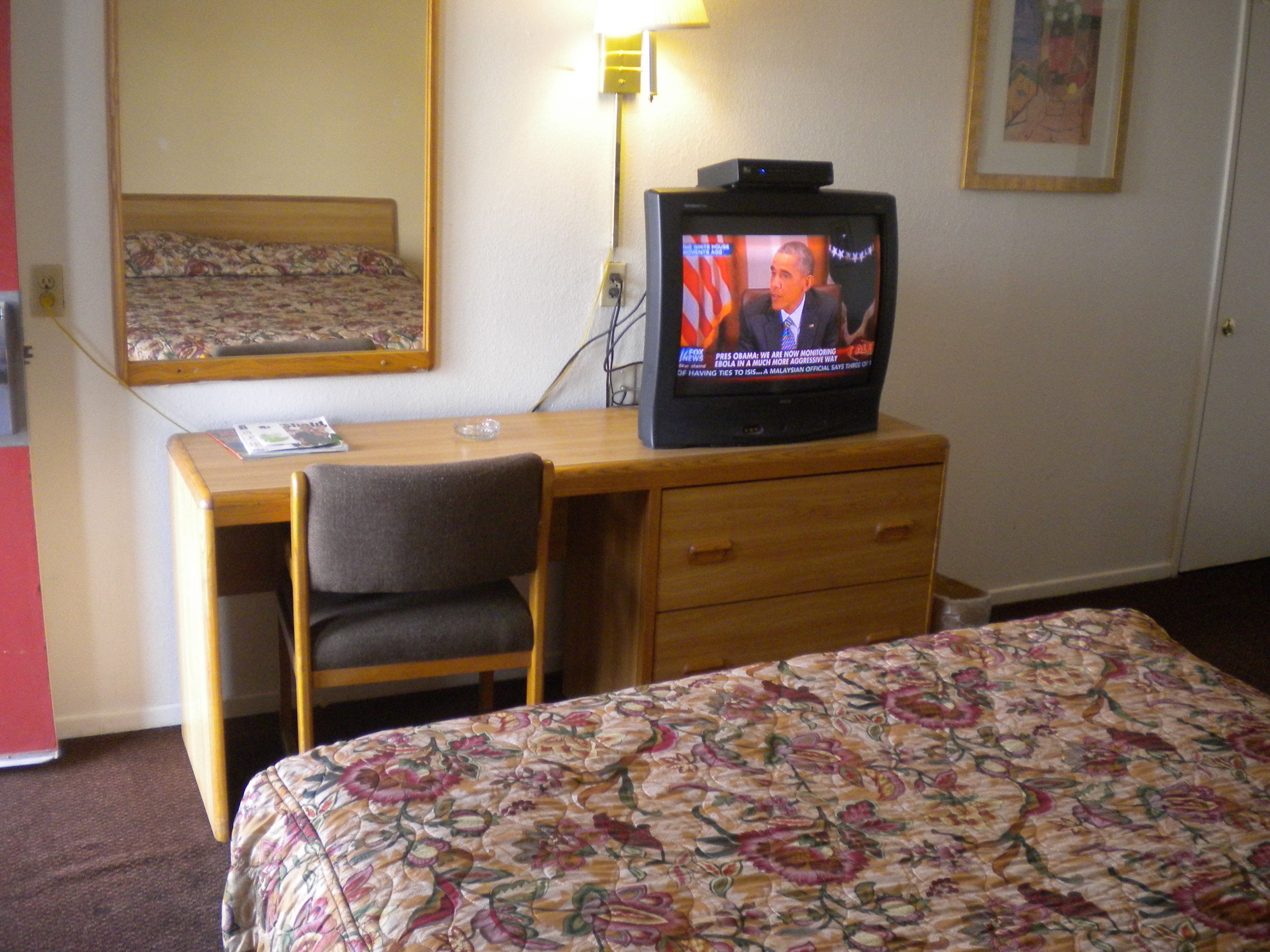 A hotel room with a wooden desk, a television, a chair, and a bed with a floral bedspread.
